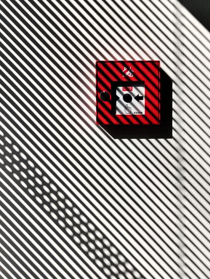 A fire alarm with blinds throwing diagonal shades across it.