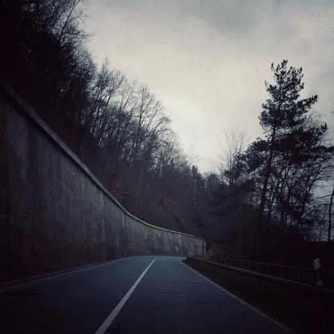 Straße durch Wald, entlang einer Mauer.