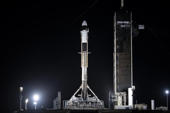 A tall black and white rocket stands ready to launch, with the night sky behind it.